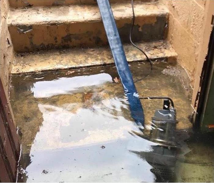 A submersible pump, blue hose, extracting water from a cellar exterior entrance